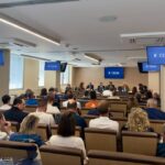Una sala per convegni con vari monitor e il pubblico ripreso di schiena