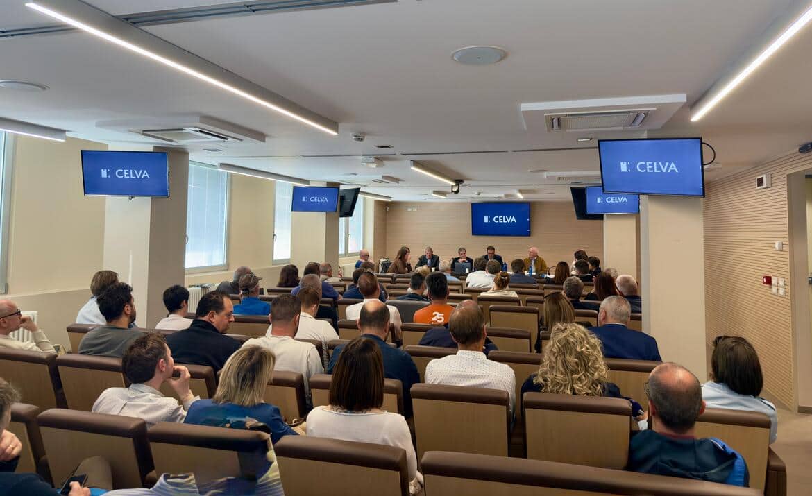 Una sala per convegni con vari monitor e il pubblico ripreso di schiena
