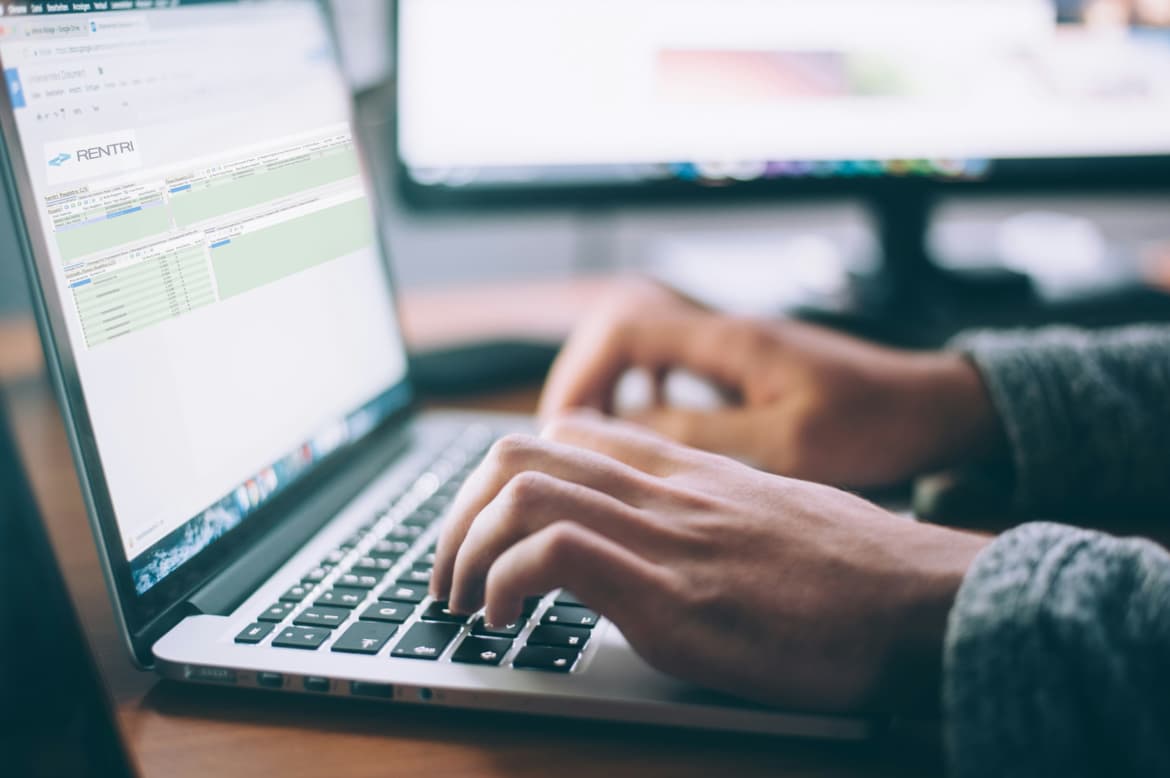 Le mani di una persona che digita su un portatile e sfocato sullo sfondo il monitor di un computer